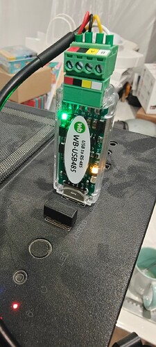 На изображении показано устройство WB-USB485, подключенное к поверхности с несколькими кнопками и индикаторами, среди которых виден зелёный светодиод. (Captioned by AI)