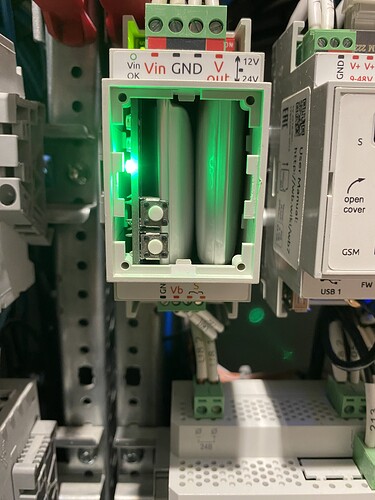 На изображении показан блок питания с зелёным индикатором, установленный в электрическую панель. (Captioned by AI)