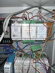 На изображении представлены модули управления, такие как WB-MIO-E, WBIO-DO-10A-8 и WBIO-DH-DVD-8, подключенные к проводам и размещенные внутри электрического шкафа. (Captioned by AI)