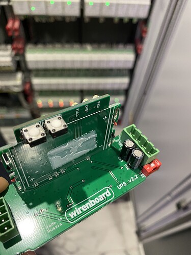 На изображении представлен электрический платформа Wirenboard с двумя разъемами и конденсаторами, держащее ее на фоне шкафов с оборудованием. (Captioned by AI)