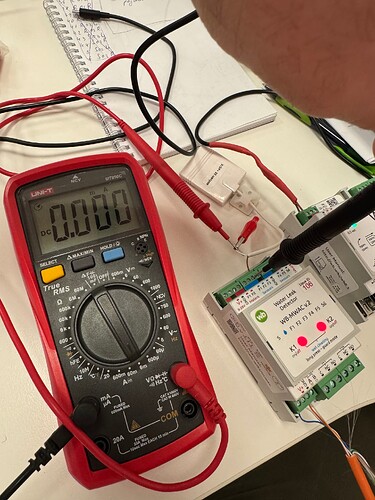 На изображении показан цифровой мультиметр, измеряющий напряжение на электрическом устройстве, с подключенными измерительными проводами. (Captioned by AI)