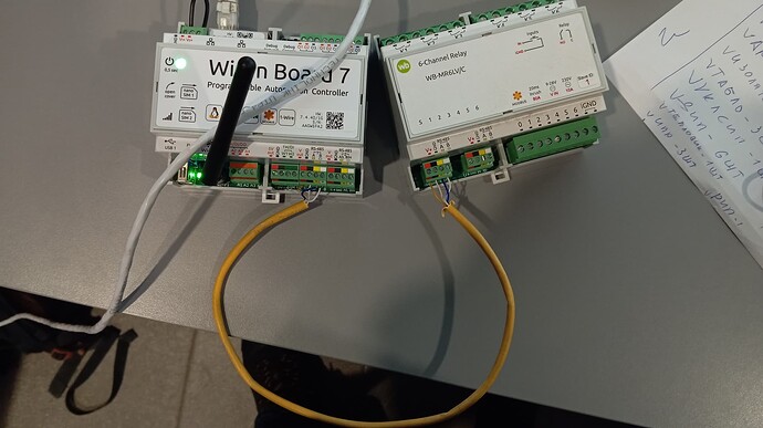 На изображении два программируемых контроллера, соединенных между собой проводами, расположенные на столе. (Captioned by AI)