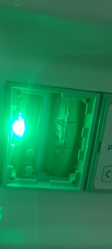 Изображение показывает светодиодный индикатор ярко-зеленого цвета внутри электрической коробки. (Captioned by AI)