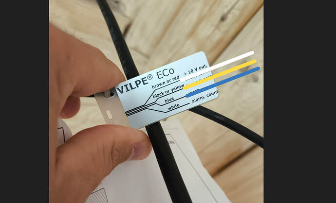 На изображении представлена рука, держащая пластиковую табличку с надписью "VILPE ECO", указывающую на назначение проводов разных цветов и их подключения. (Captioned by AI)