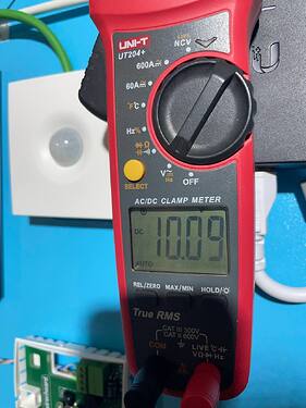 На изображении представлен цифровой клещевой мультиметр UNI-T UT204+, показывающий значение 10.09 в режиме измерения постоянного тока. (Captioned by AI)
