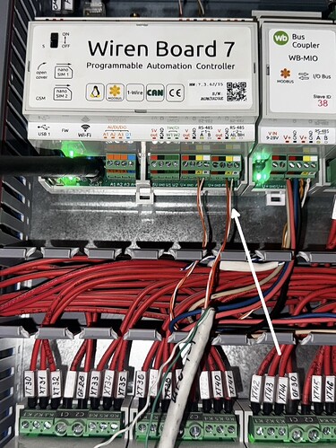 На изображении показан контроллер автоматизации Wiren Board 7 с подключенными проводами и светодиодами, расположенный внутри электронного шкафа. (Captioned by AI)