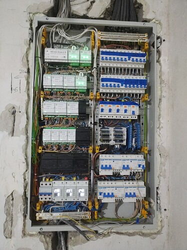 На изображении показан электрический щит с множеством проводов и устройствами управления, установленных в металлическом корпусе на стене. (Captioned by AI)