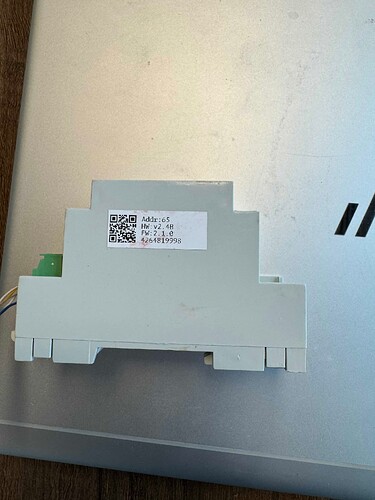 На изображении видно устройство белого цвета с таблицей данных и QR-кодом, размещенное на поверхности ноутбука. (Captioned by AI)