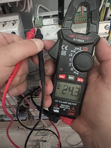 На изображении человек держит мультиметр KBT Progres KT200A с показанием 24.3, подключая тестеры к электрической системе. (Captioned by AI)