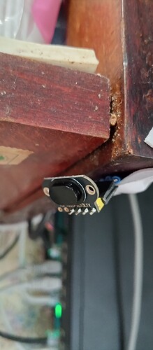 На изображении показан маленький датчик, установленный на деревянной поверхности стола, рядом с проводами и другим оборудованием. (Captioned by AI)